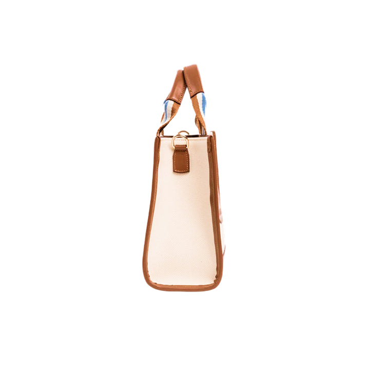 Side view of the JOCOSA Club Tote bag in ivory canvas with camel leather trim, camel, ivory and blue striped handles and gold-tone hardware.