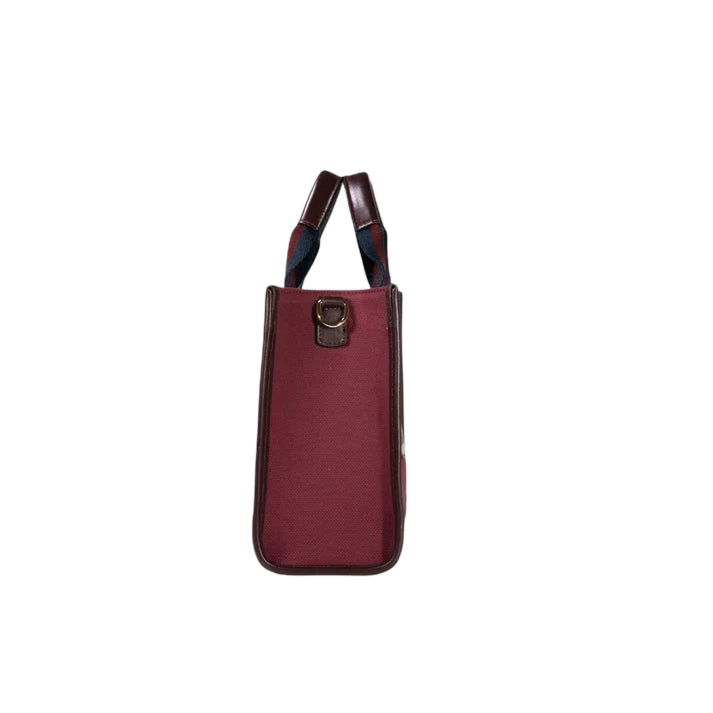 Side view of the JOCOSA Club Tote bag in bordeaux canvas with bordeaux leather trim, navy and bordeaux striped handles and gold-tone hardware.