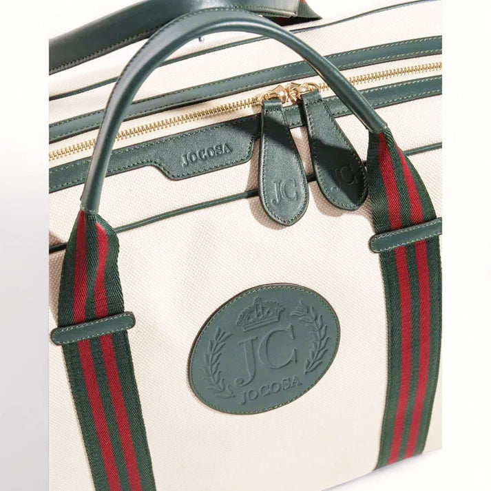 Close-up of the JOCOSA Club Weekender Bag in ivory canvas with green leather trim, green and bordeaux striped handles, gold-tone zippers, embossed leather zipper pulls and embossed leather logo.