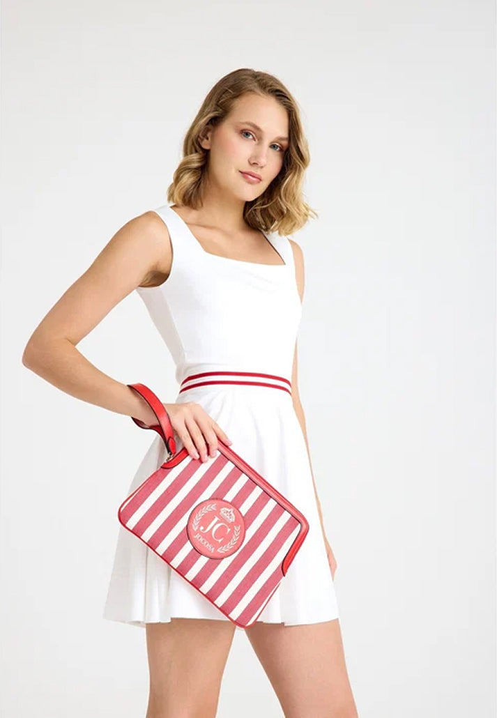 Female model wearing a white tennis outfit, carrying the JOCOSA Locker Pouch in ivory and red striped canvas with red leather trim, a wrist strap and leather logo with gold foil detailing.