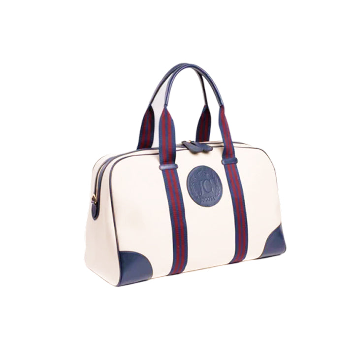 Three-quarter view of the JOCOSA Club Carryall bag in ivory canvas with navy leather trim, navy and bordeaux striped handles, gold-tone zipper hardware and embossed leather logo on the front.