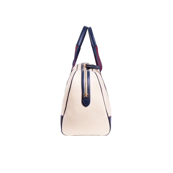 Side view of the JOCOSA Club Carryall bag in ivory canvas with navy leather trim, navy and bordeaux striped handles and gold-tone hardware.