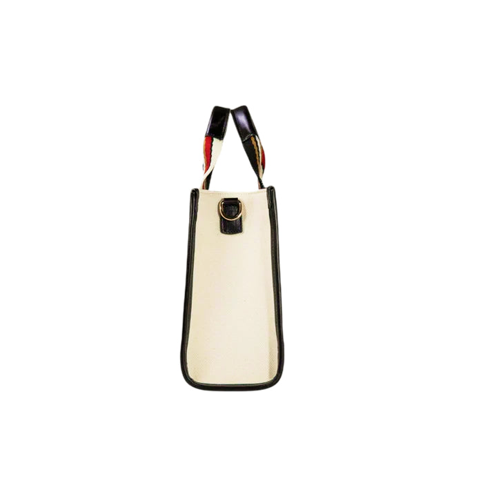Side view of the JOCOSA Club Tote bag in ivory canvas with black leather trim,  black, red and ivory striped handles and gold-tone hardware.