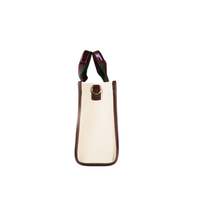 Side view of the JOCOSA Club Tote bag in ivory canvas with bordeaux leather trim, green and bordeaux striped handles and gold-tone hardware.