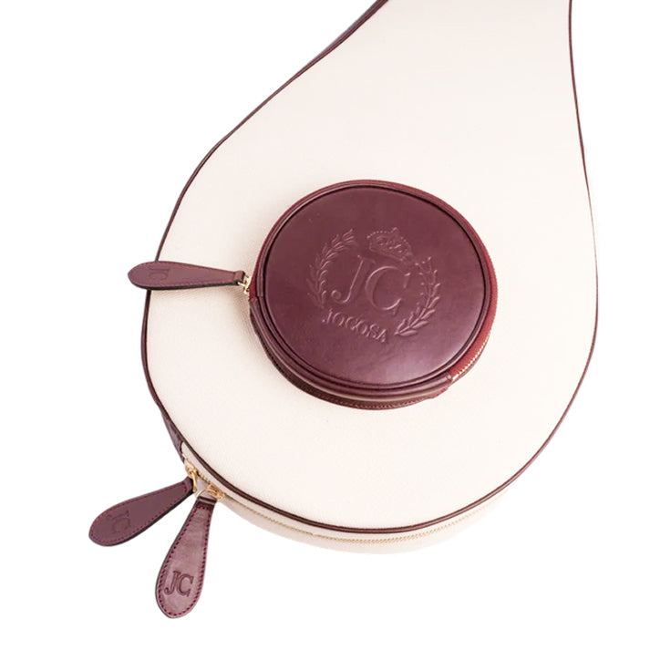 Close-up of the JOCOSA Racket Case in ivory canvas with bordeaux leather trim, round front pocket, gold-tone zippers and embossed leather logo.